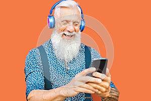 Senior man using mobile smartphone while listening music playlist with wireless headphones - Mature hipster male having fun
