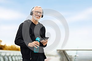 Senior man using phone while have outdoor workout, drinking water