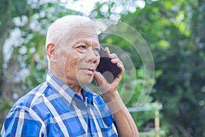 Senior man using a smartphone while standing in a garden. Space for text. Concept of aged people and technology