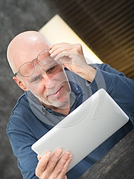 Senior man using tablet, he is having difficulties and vision problems