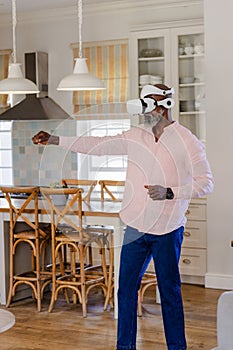 Senior man using VR headset in kitchen, engaging in virtual reality experience