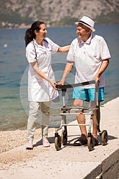 Senior man using a walker with caregiver near the sea at summer