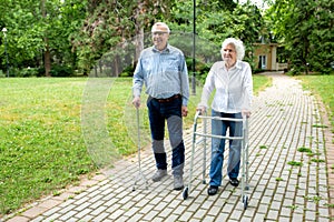 Senior man using a walking cane accompanied by a senior lady strolling with folding walker