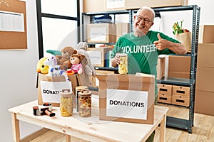 Senior man volunteer holding donations box putting food into a box smiling happy and positive, thumb up doing excellent and