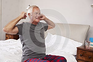 Senior Man Waking Up And Stretching In Bedroom