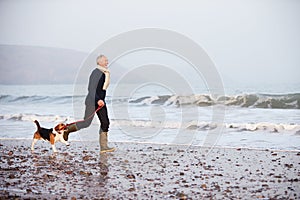 Senior Man Walking Along Winter Beach With Pet Dog