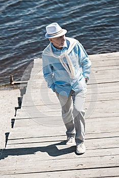 Senior man walking by pavement on the riverside at daytime