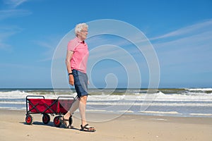 Senior man walking with red cart at beach