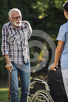 Senior man walking with stick toward wheelchair