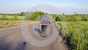 Senior man with walking stick walking away on a country road