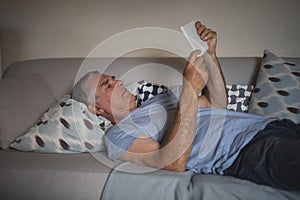 Senior man watching digital tablet while lying on sofa