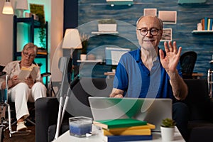 Senior man waving at video call conference on laptop
