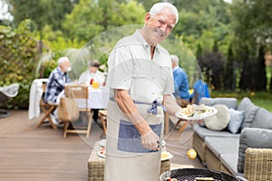 Senior man wearing apron and holding plate of food during garden hoopla