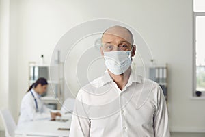 Senior man wearing protective mask on visit to doctor at hospital, blank space. Patient and medical specialist at clinic