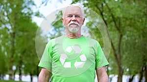 Senior man wearing recycling symbol t-shirt looking at camera, forest background