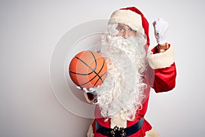 Senior man wearing Santa Claus costume holding basketball ball over isolated white background annoyed and frustrated shouting with