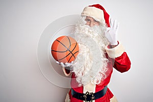 Senior man wearing Santa Claus costume holding basketball ball over isolated white background doing ok sign with fingers,