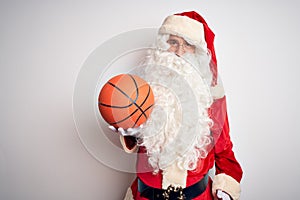 Senior man wearing Santa Claus costume holding basketball ball over isolated white background with a happy face standing and