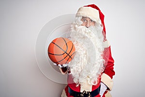 Senior man wearing Santa Claus costume holding basketball ball over isolated white background scared in shock with a surprise
