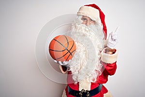 Senior man wearing Santa Claus costume holding basketball ball over isolated white background very happy pointing with hand and