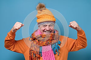 Senior man wearing several hats ans scarfs celebrating success with two fists up