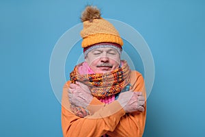 Senior man wearing several hats and scarfs freezing because of cold weather.
