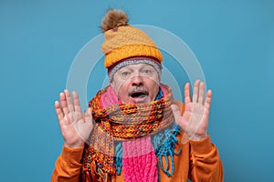 Senior man wearing several scarfs and hats being afraid and shocked