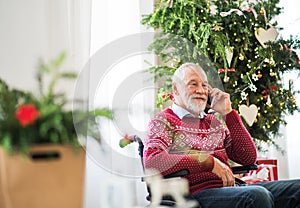 A senior man in wheelchair with mobile phone at home at Christmas time, making a phone call.