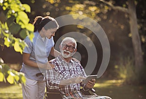 Senior man in wheelchair and nurse looking at tablet