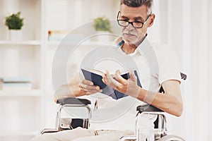 Senior Man in Wheelchair Reading Book at Home.