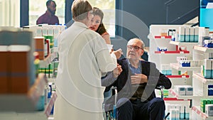 Senior man in wheelchair and social caretaker talking to pharmacist