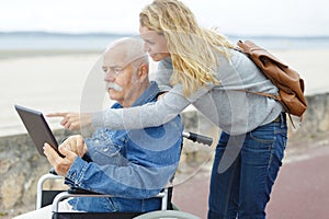 senior man in wheelchair with tablet outdoors