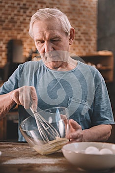 Senior man whipping cream with whisk in glass bowl