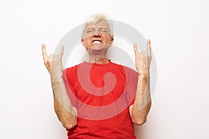 Senior man with white hair wearing red t-shirt shouting with crazy expression doing rock symbol with hands up.