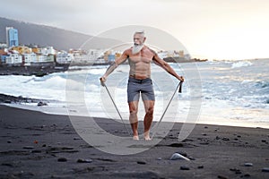 Senior man with white stylish beard exercising on the beach. Summer vacation workout