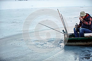 Senior man in winter fishing drink tea on frozen lake