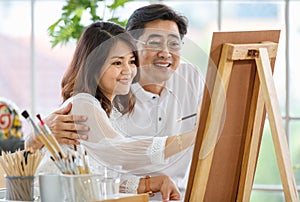 Senior man and woman couple, husband and wife, painting image together in home gallery with warm and happy circumstance. The man