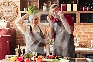 Senior man and woman having fun with vegetables at kitchen