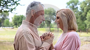 Senior man and woman holding hands, looking each other with love, happy couple