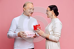 Senior man and woman, married couple giving each other presents, celebrating holiday, anniversary against pink