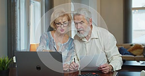 Senior man and woman paying bills and managing budget. Mature worried couple sitting and managing expenses at home.