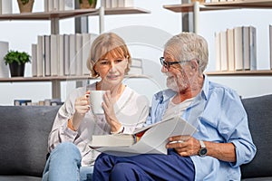Senior man and woman reading a book and enjoying coffee, Cheerful couple spending time together in the living room