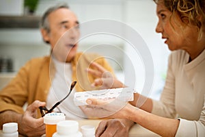 Senior man and woman taking medicine in morning, wife giving daily pills to her husband, kitchen interior