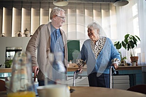 Senior man and woman walking with walker indoors in retirement nursing hme.
