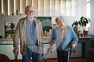 Senior man and woman walking with walker indoors in retirement nursing hme.