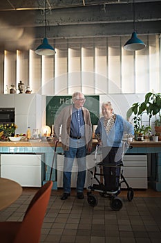 Senior man and woman walking with walker indoors in retirement nursing hme.