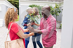 Senior man and woman welcoming multiracial friends at entrance during house party