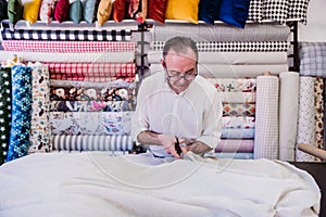 senior man working in atelier cutting curtains. Small business