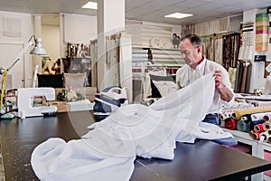 senior man working in atelier ironing curtains. Small business