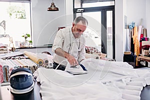 senior man working in atelier ironing curtains. Small business